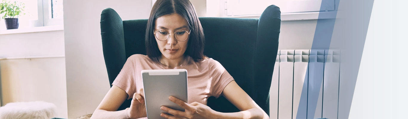 woman sitting down in a chair using a tablet with a dog on her lap