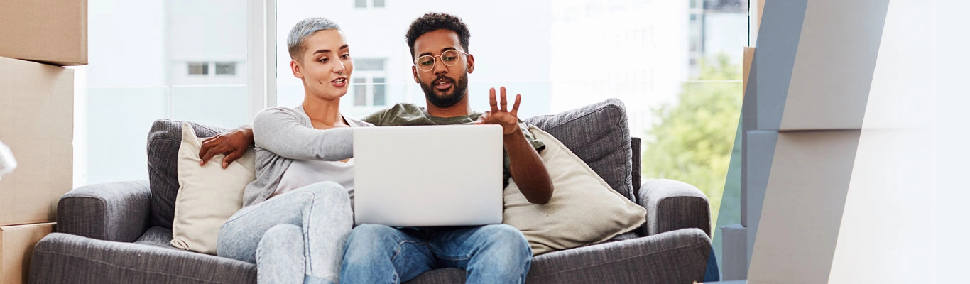 Couple on couch with laptop and moving boxes